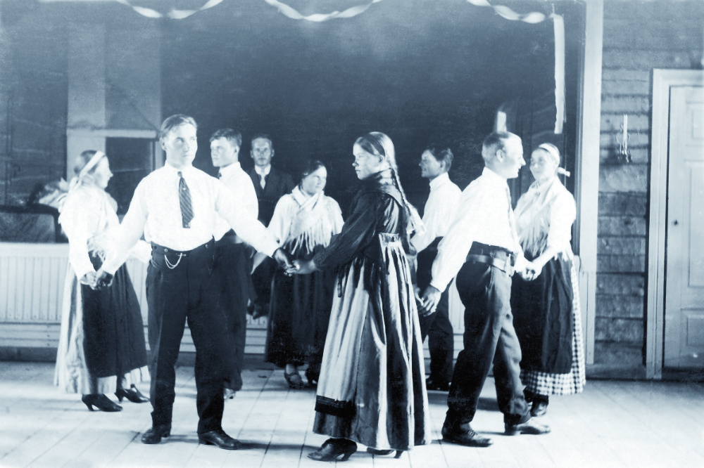 Historiallinen kuva, jossa aikuisia kansanomaisissa asuissa piirissä tanssimassa.