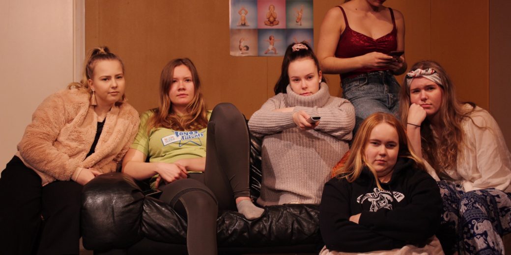 Kuvassa sohvalla istuskelee kuusi nuorta naista.