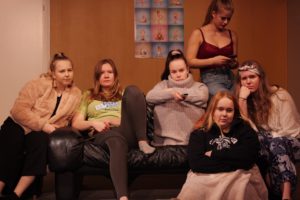 Kuvassa sohvalla istuskelee kuusi nuorta naista.