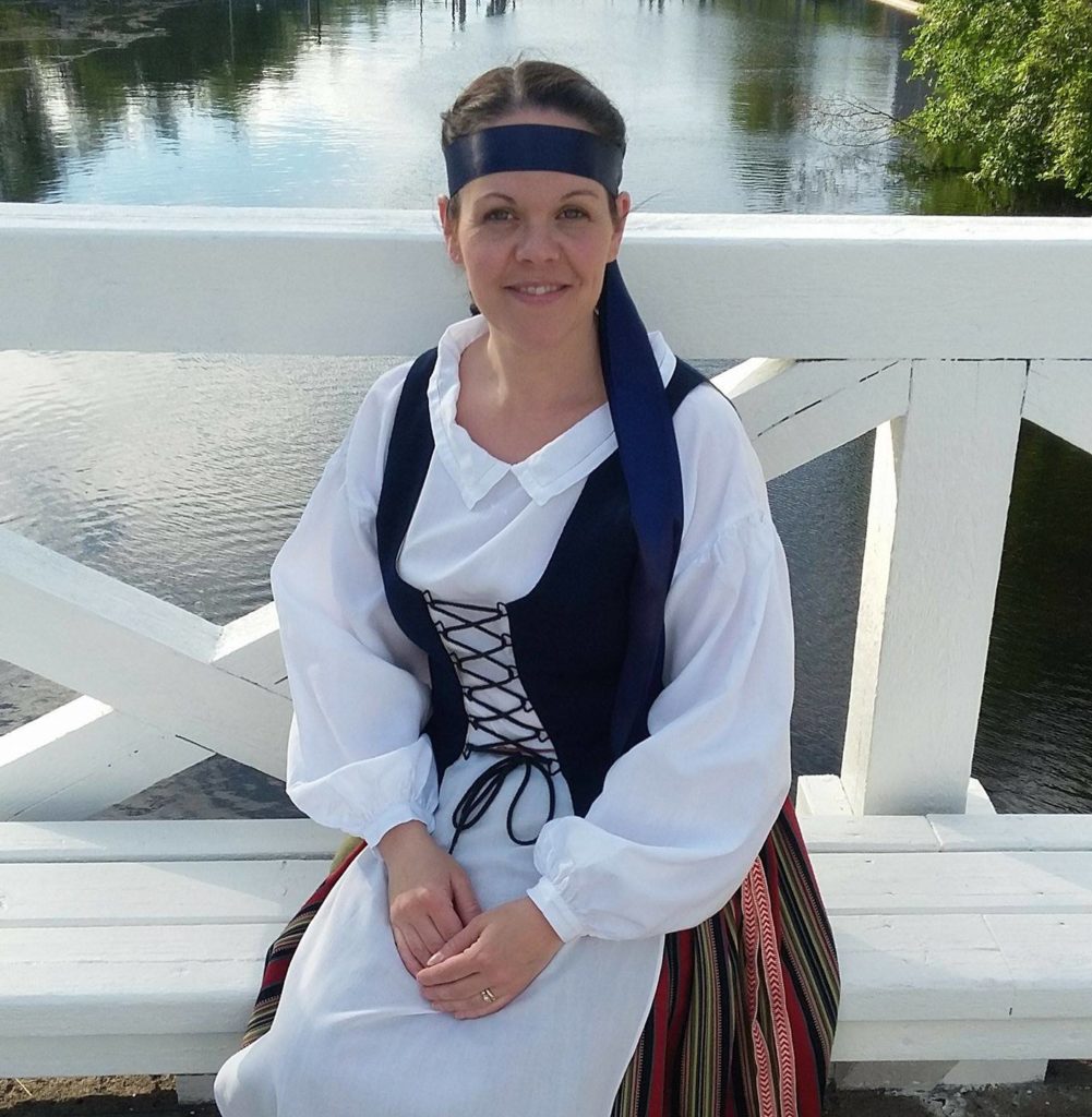 Marika Timonen kansallispuvussa istumassa Penttilän sillalla. 
